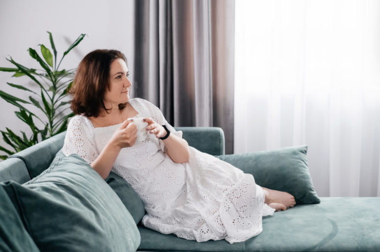 Woman relaxing on a sofa with a cup of coffee, enjoying a calm morning in her home after childbirth