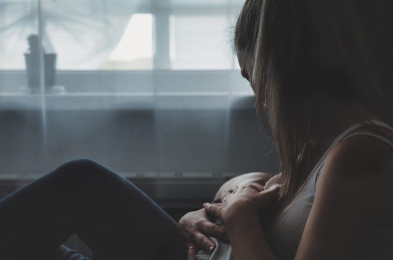 Mother breastfeeding her newborn baby at home, sitting quietly near a window in natural light