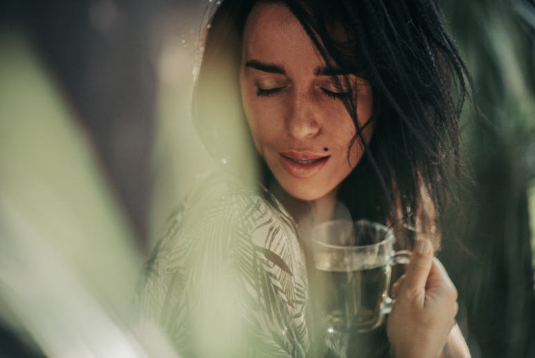 امرأة تستمتع بفنجان من الشاي العشبي وعيناها مغمضتان، ترمز إلى التغذية والاسترخاء وصحة الخصوبة الطبيعية من خلال العادات الصحية.