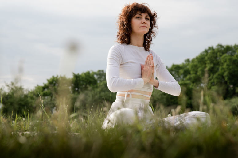 امرأة تستلقي على العشب مرتدية ملابس بيضاء، ترمز إلى الهدوء والتوازن ودعم الخصوبة الطبيعي من خلال الاسترخاء والعناية بالنفس.