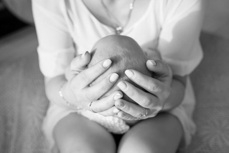Close-up of a mother’s hands gently cradling her newborn’s head, symbolizing care and tenderness