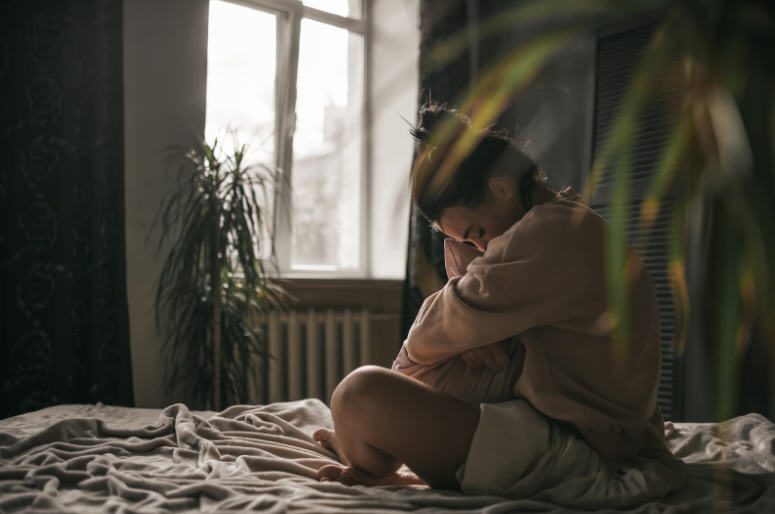 Woman sitting cross-legged on her bed, hugging a pillow and smiling softly in a peaceful morning moment