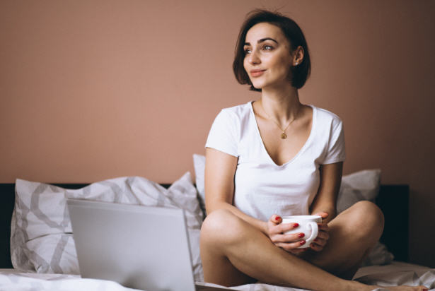 Woman sitting on her bed holding a cup of coffee, symbolizing slow mornings and fatigue associated with hormonal shifts.