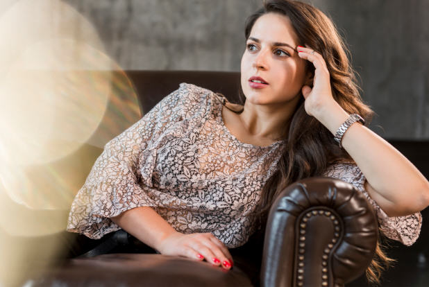 Woman sitting thoughtfully on a brown leather sofa, illustrating mood changes often linked to hormonal imbalance.